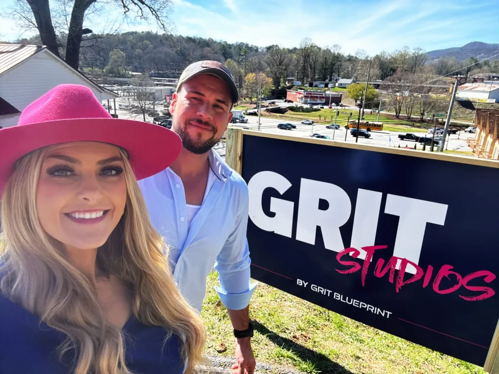 Stefanie Couch and her husband, Ben, smiling beside the Grit Studios by Grit Blueprint sign