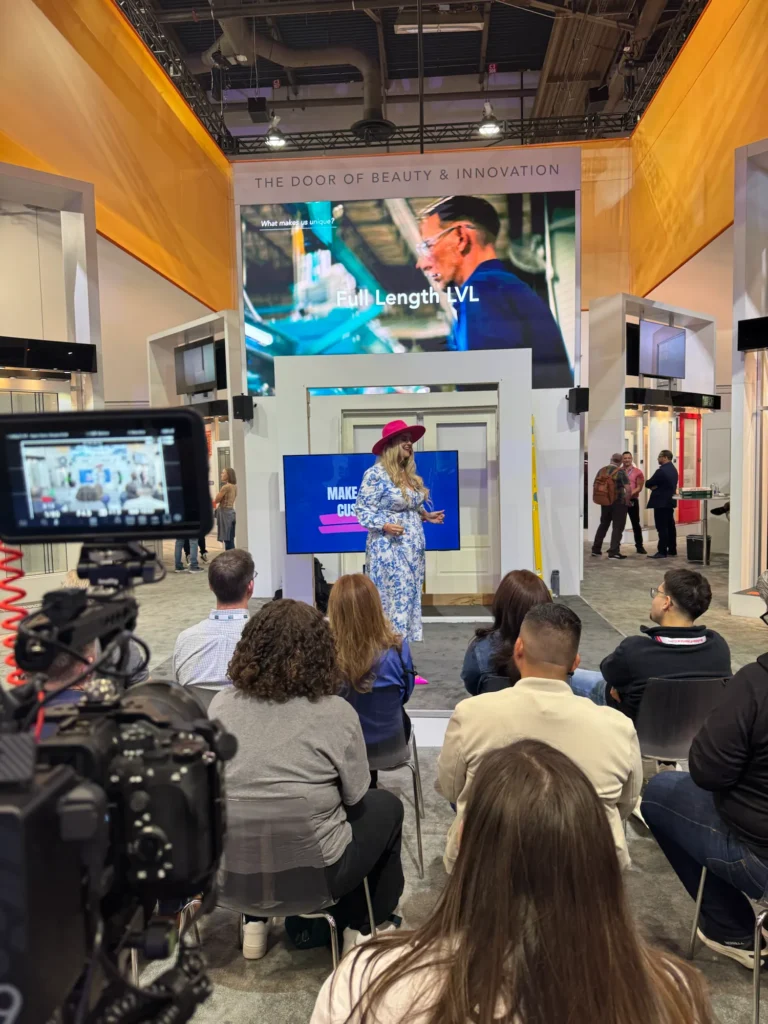 Stefanie Couch speaking at the Plastpro booth at IBS 2025, a camera and audience in front