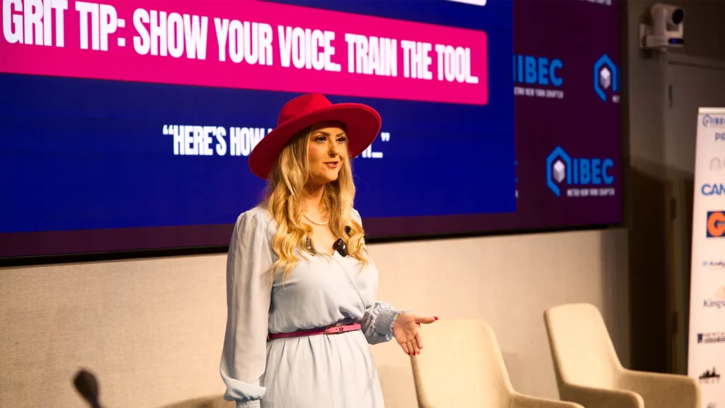 Stefanie Couch smiling on stage beside a Grit Tip slide at IIBEC Metro New York