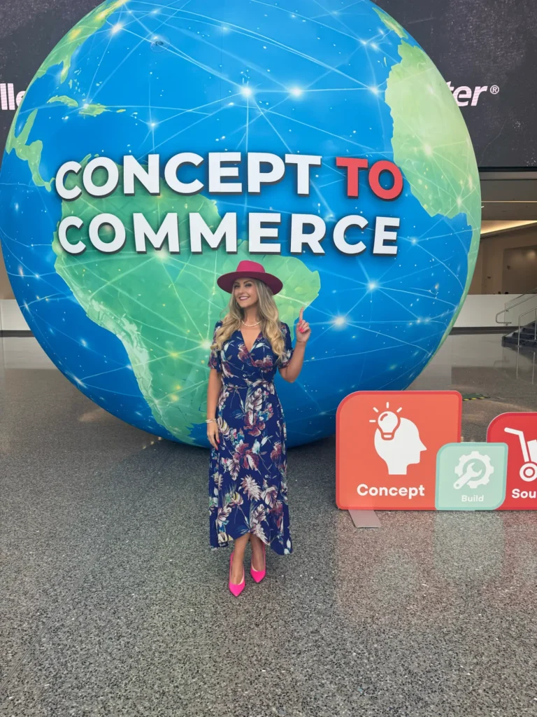 Stefanie Couch pointing up beside the Concept to Commerce globe at the National Hardware Show