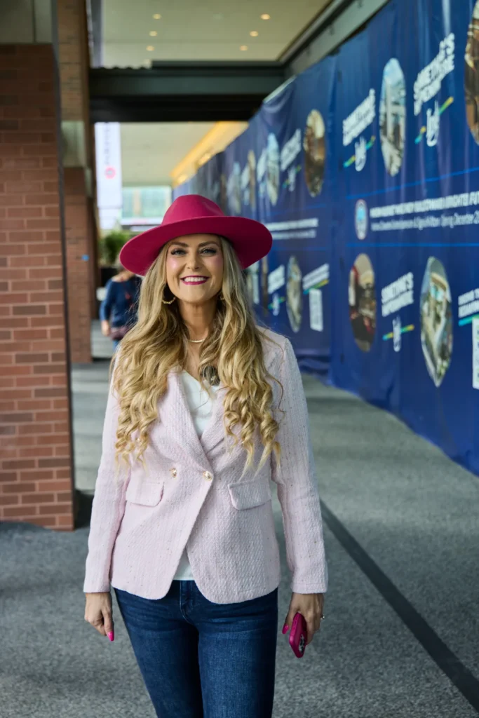 Smiling in a pink tweed blazer and pink hat, Stefanie in a convention center corridor at Do it Best Fall Market 2026