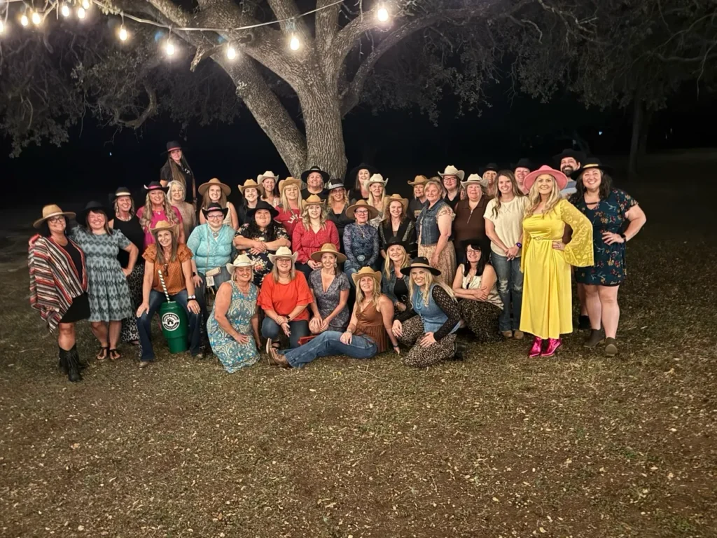 Stefanie Couch with a large group of women in western hats under a big tree strung with lights at the Nation’s Best Women’s Leadership Retreat 2025