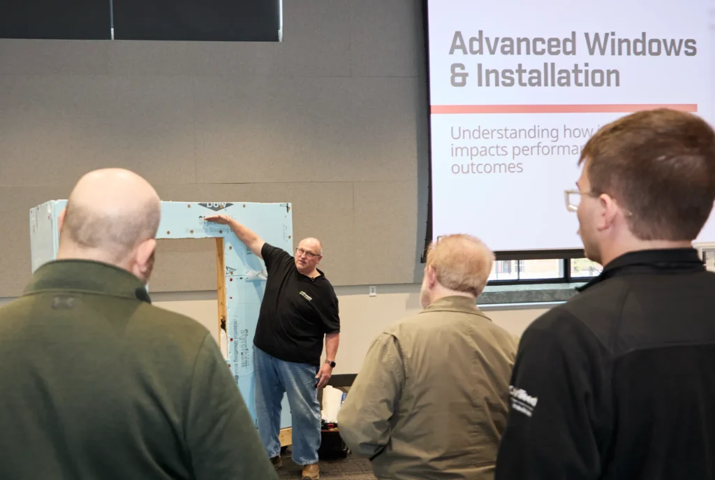 Attendees watch a window installation demo beneath the Advanced Windows & Installation slide at the Do it Best LBM Millwork Academy