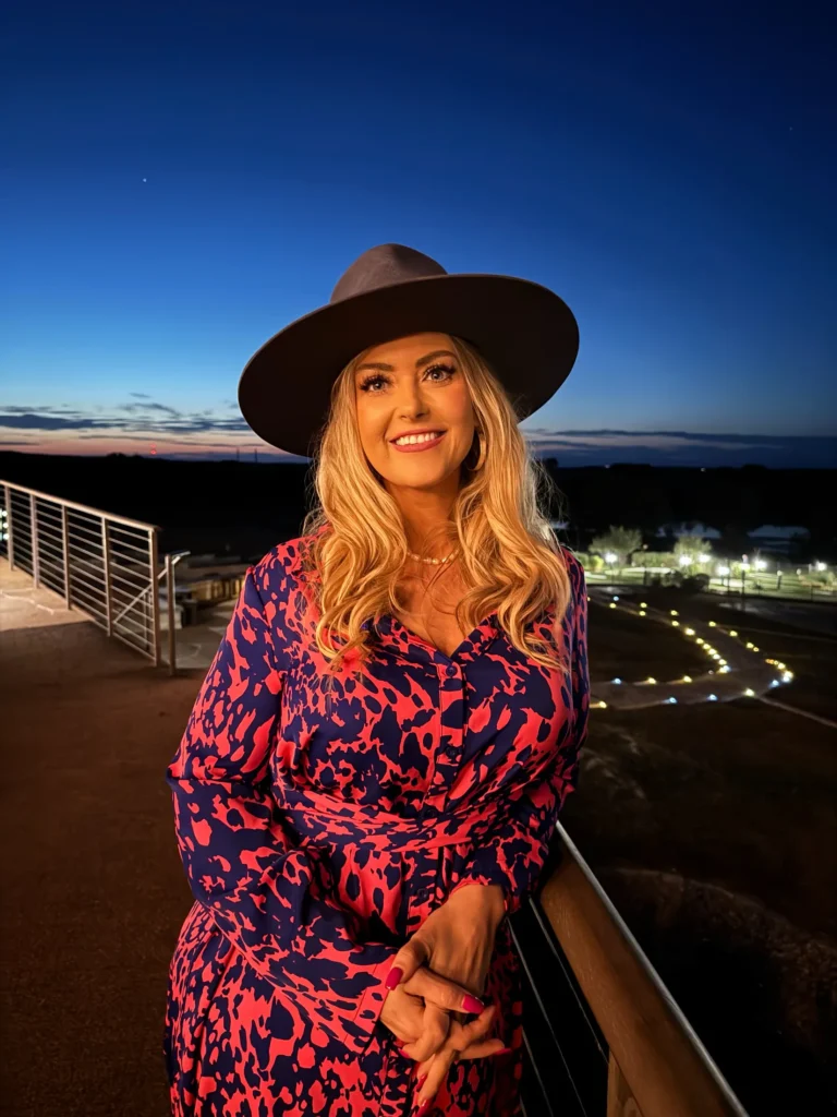 Stefanie Couch in a brown hat on a balcony at dusk during the Nation’s Best Women’s Leadership Retreat