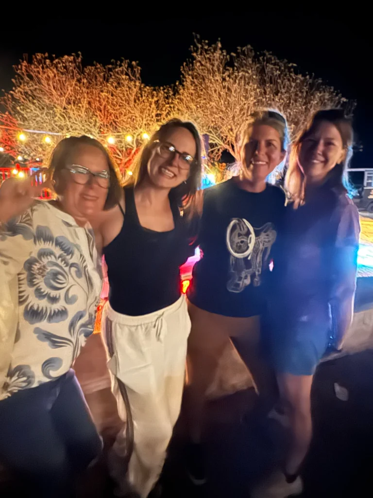 Four retreat attendees smile under string lights at an evening gathering