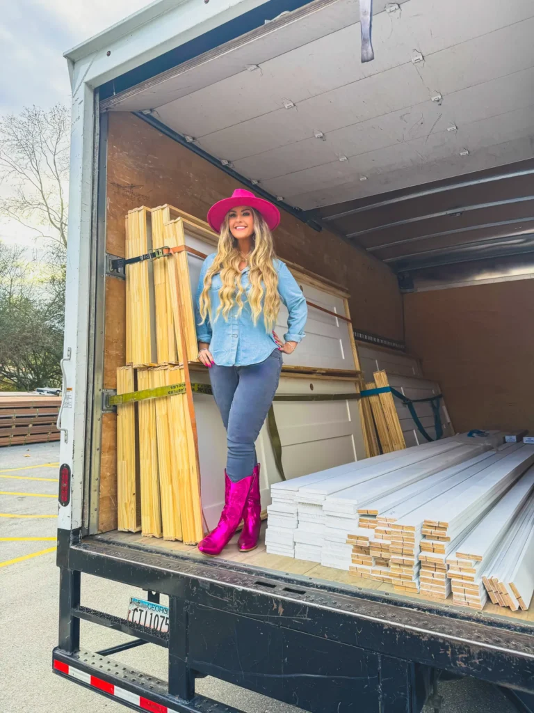 Stefanie Couch in a pink hat and pink boots standing in a box truck loaded with lumber and trim