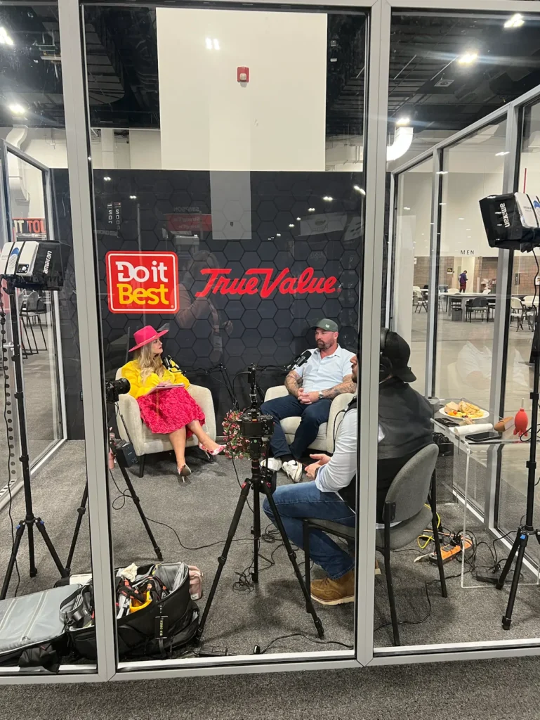 Stefanie Couch's podcast conversation inside a glass booth on a trade show floor, the crew outside